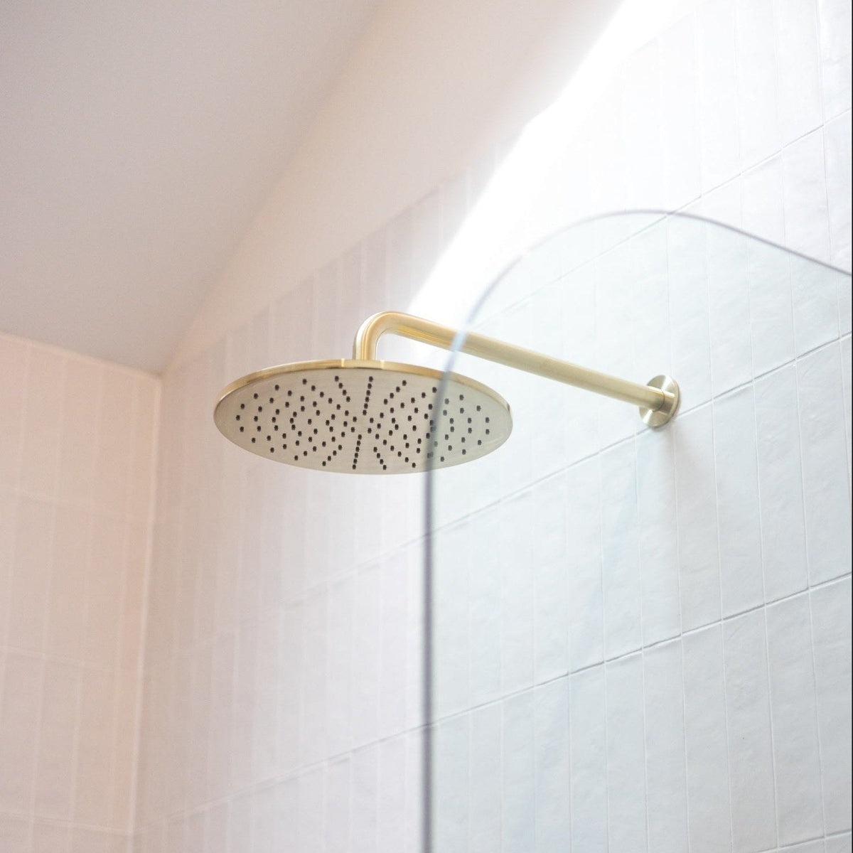 Brushed bronze round rain shower head in a bright white tiled shower