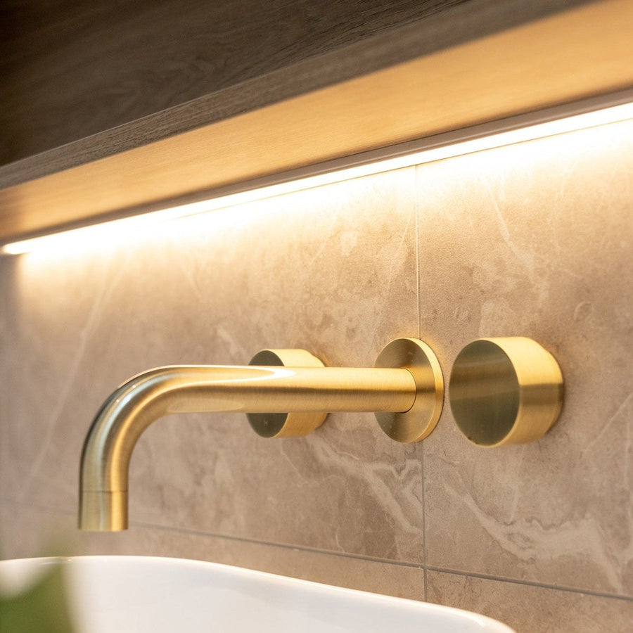 Brushed bronze wall basin taps above a stone basin in a warm, softly lit bathroom