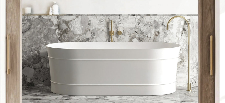 Banded white freestanding bath with a brushed brass floor mounted bath filler against a stone look wall