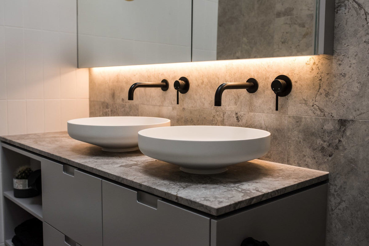Twin round vessel basins with matte black wall mixers on a stone topped vanity