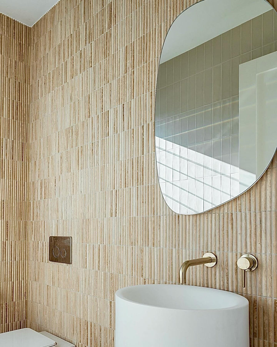 Vertical finger mosaic tiles behind a pedestal basin and a brushed brass wall mixer