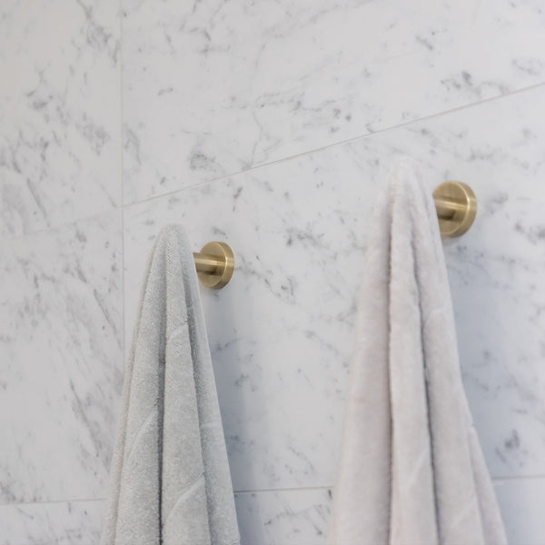 Brushed bronze robe hooks holding soft towels on a marble wall