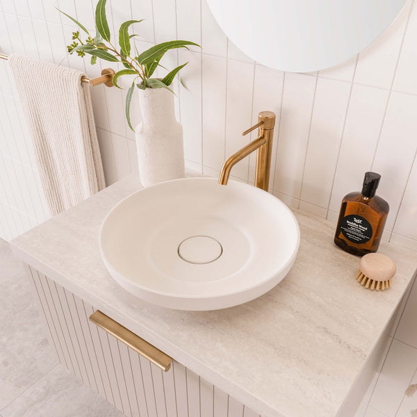 White round above-counter basin with brushed brass mixer on a stone vanity top