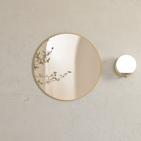 Round brushed gold framed mirror beside a globe wall light