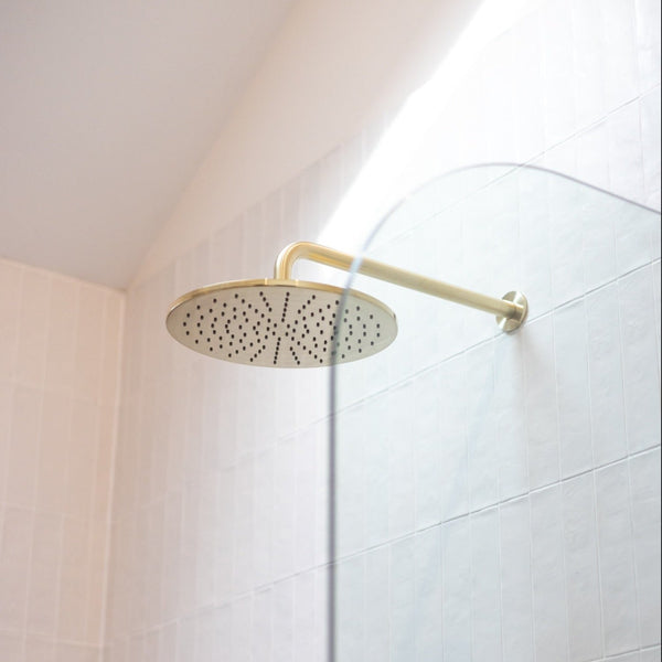 Brushed bronze round rain shower head in a bright white tiled shower