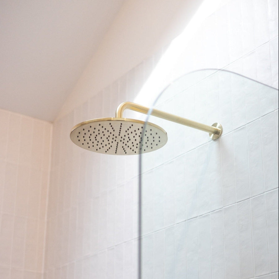 Brushed bronze round rain shower head in a bright white tiled shower