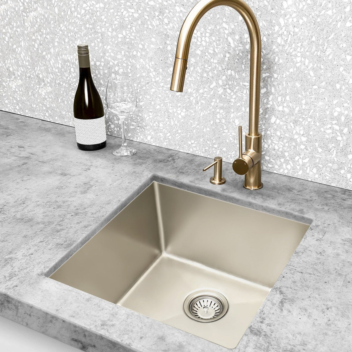Brushed gold gooseneck kitchen mixer over a champagne undermount sink with a terrazzo look splashback