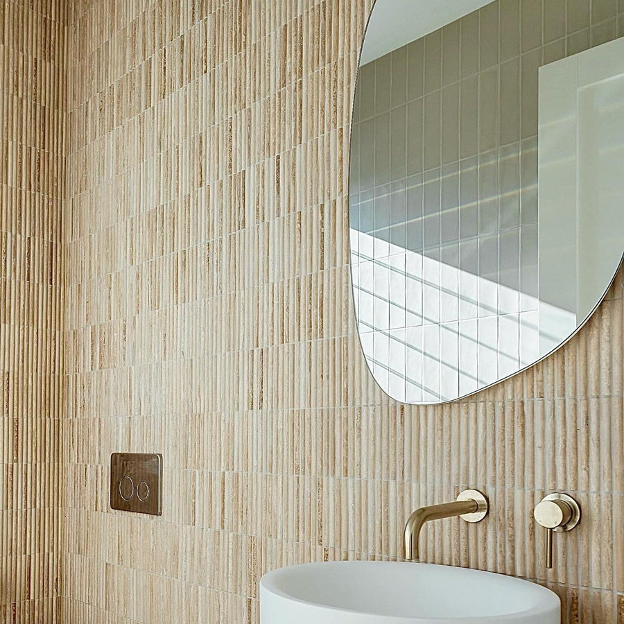 Travertine bamboo mosaic feature wall with a brushed brass wall mixer and an organic shaped mirror