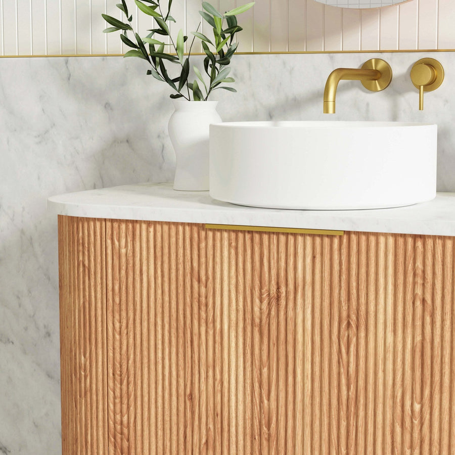 Fluted timber vanity with a white vessel basin, brushed brass wall mixer and marble look walls