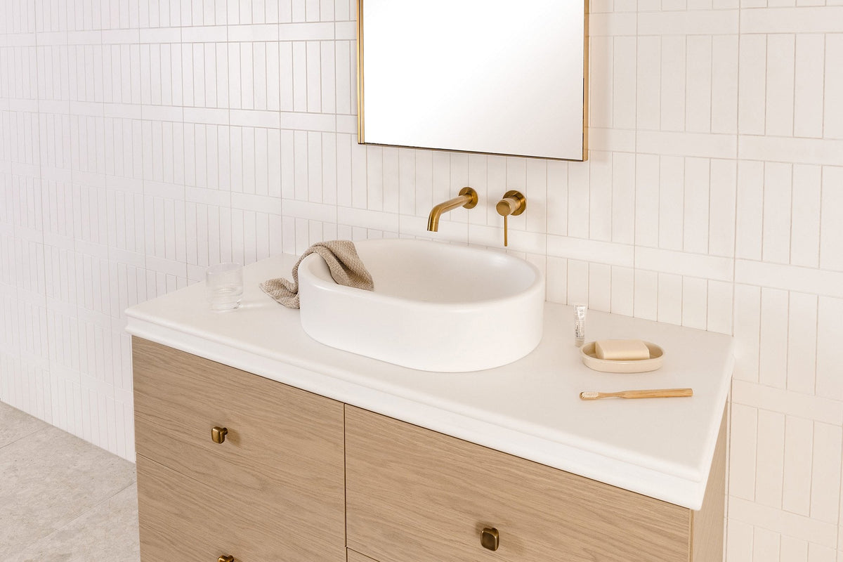 Timber vanity with a white stone top, round vessel basin and brushed brass wall mixer