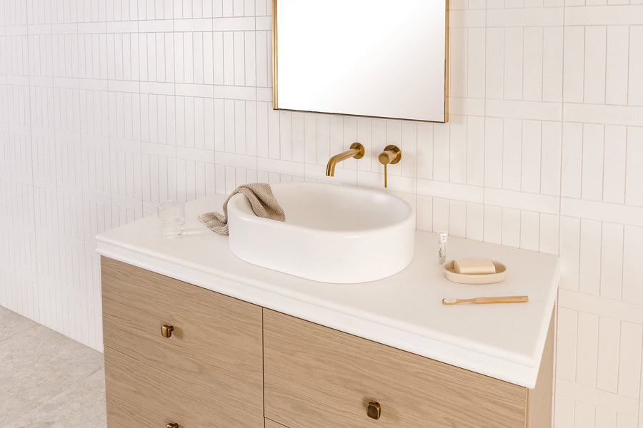 Timber vanity with a white stone top, round vessel basin and brushed brass wall mixer