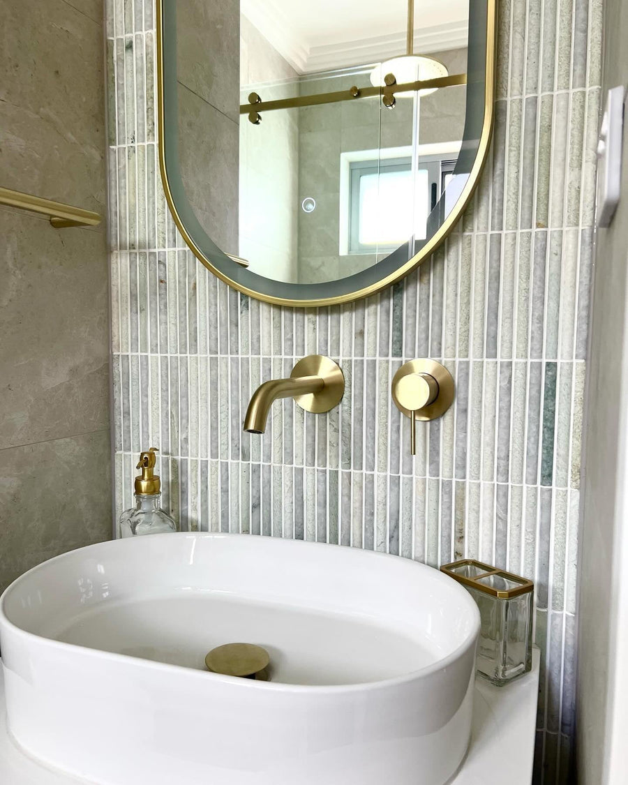 Green vertical gloss tiles behind an oval brass mirror and a white vessel basin