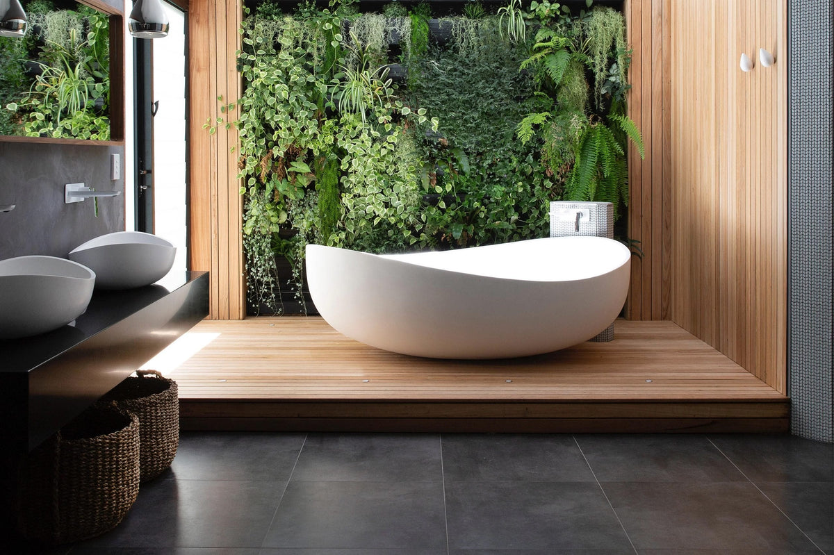 Sculpted white freestanding bath on a timber platform in front of a green living wall