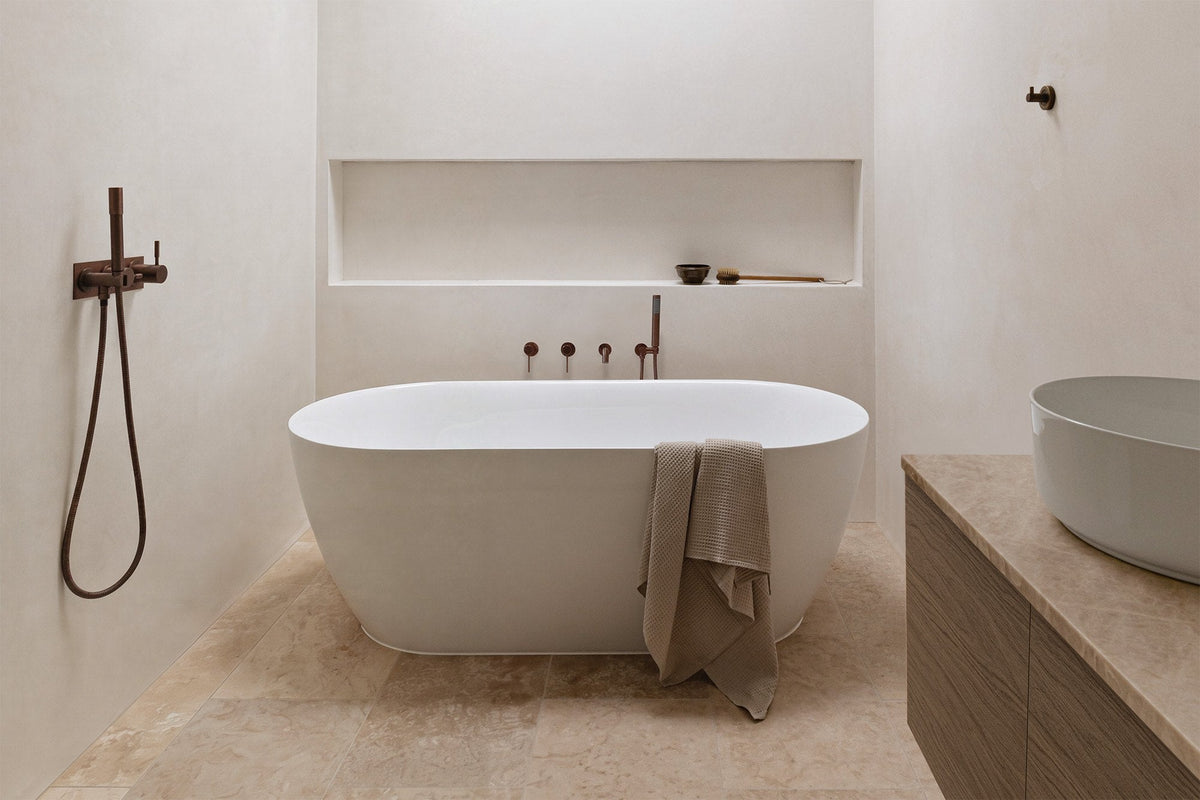 Freestanding oval bath with bronze wall taps, travertine floor tiles and a timber vanity