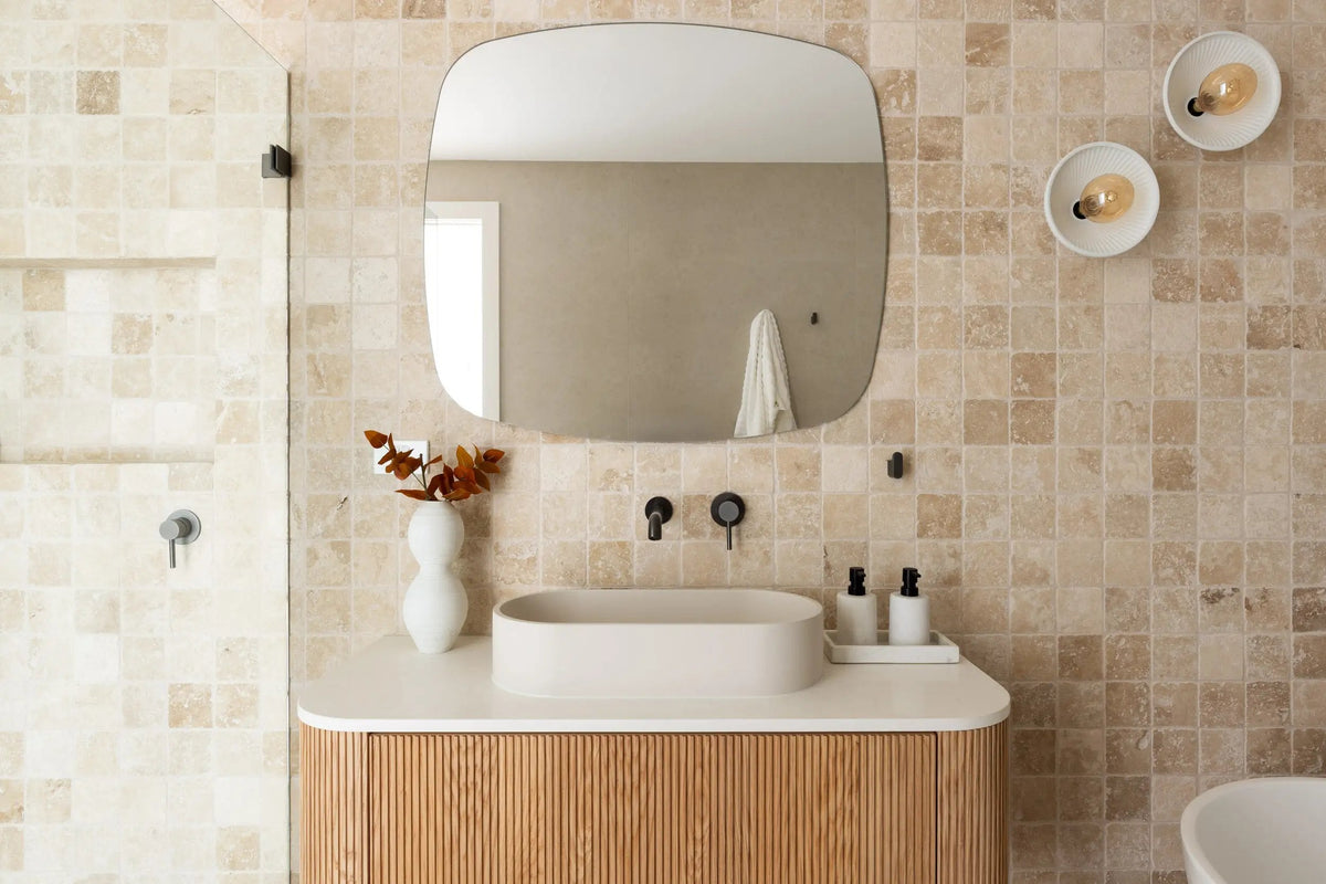 Honed stone mosaic bathroom wall with a curved timber vanity and a soft edged mirror