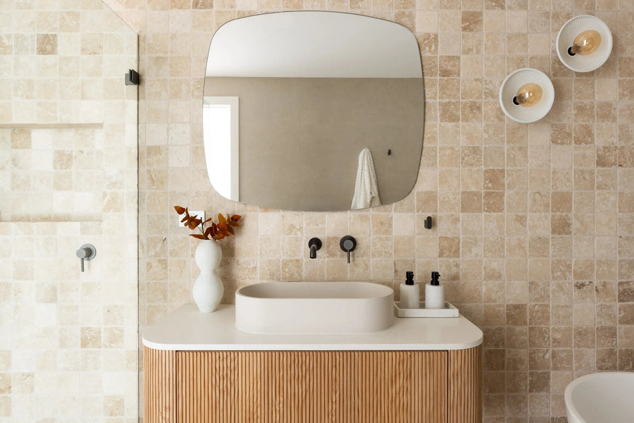 Honed stone mosaic bathroom wall with a curved timber vanity and a soft edged mirror