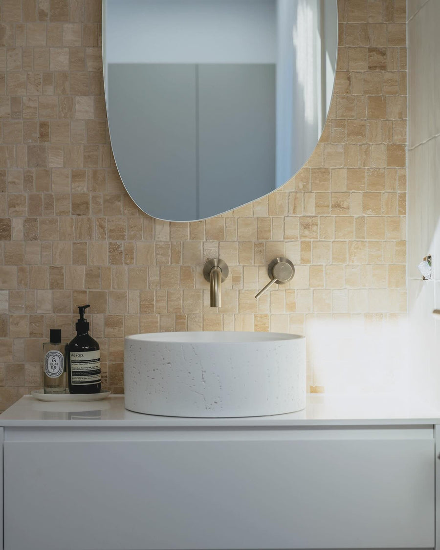 Split stone mosaic wall above a white vanity with a round vessel basin